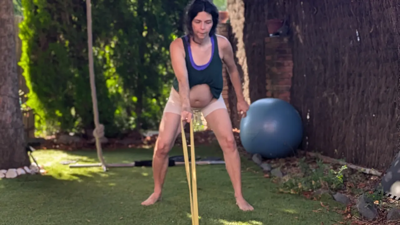 Una dona embarassada fa un exercici de força amb una goma elàstica en un jardí.